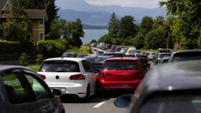 Stau mit weißen und roten Autos auf einer Straße vor einem See und Bergen