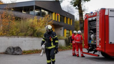 Feuerwehrmann in voller Schutzausrüstung vor einem modernen Gebäude und einem roten Einsatzfahrzeug