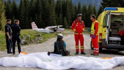 Rettungskräfte und Polizei stehen neben einem ausgebreiteten Paraglider auf einer Forststraße