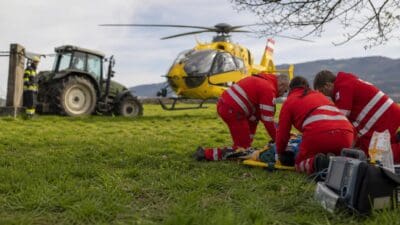Sanitäter behandeln verletzten Mann auf Trage vor gelbem Rettungshubschrauber auf Wiese