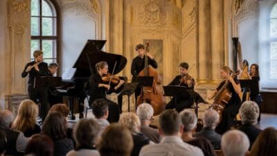 Musiker spielen Klavier Violine Cello und Kontrabass vor Publikum in prachtvollem Saal