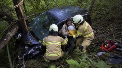 Zwei Feuerwehrleute helfen einer Mutter mit Kleinkind aus einem verunglückten Auto im Wald