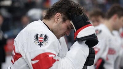 Enttäuschter österreichischer Eishockeyspieler mit gesenktem Kopf und Helm in der Hand