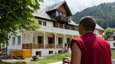 Buddhistischer Mönch in roten Roben vor einem renovierten Gebäude mit Baustelle in Oberzeiring