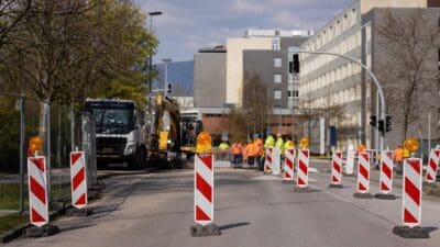 Bauarbeiter in Warnwesten neben einem Bagger auf einer abgesperrten Straße in Klagenfurt