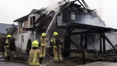 Feuerwehrleute löschen mit Wasserschlauch einen brennenden Dachstuhl eines Einfamilienhauses