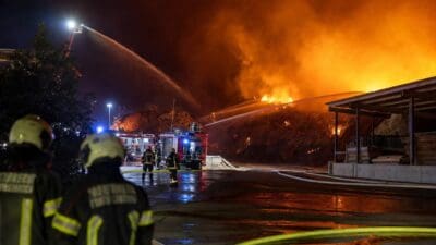 Feuerwehrleute bekämpfen bei Nacht einen Großbrand in einem Sägewerk mit Löschfahrzeugen