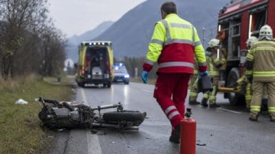 Umgestürztes Motorrad auf der Straße neben Rettungskräften und Feuerwehrfahrzeug