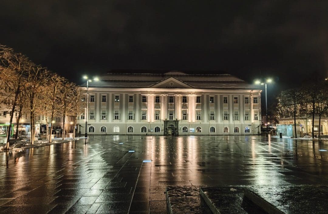 Das hell erleuchtete Rathaus Klagenfurt bei Nacht auf einem nassen Platz mit Lichtreflexionen