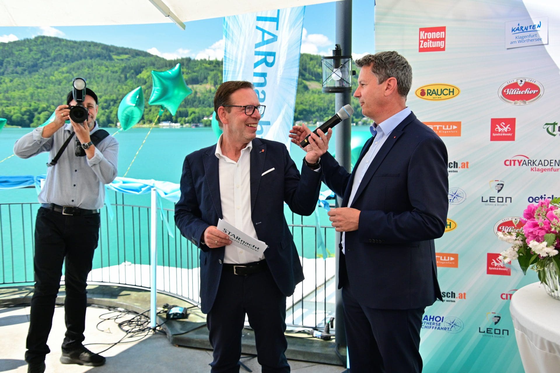 Zwei Männer in Anzügen bei einer Veranstaltung am Wörthersee mit Fotograf im Hintergrund