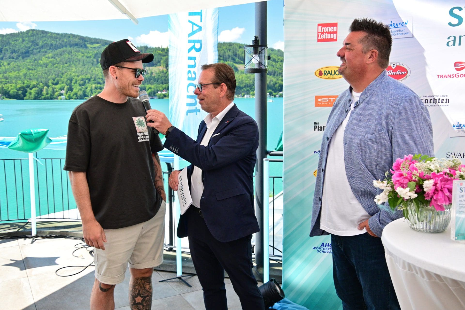 Moderator im Anzug interviewt Mann im schwarzen T-Shirt mit Cap am Wörthersee