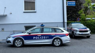 Zwei Polizeifahrzeuge parken vor einem hellen Gebäude mit Polizeischild