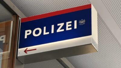 Blaues Polizeischild mit weißer Aufschrift und rotem Pfeil nach links