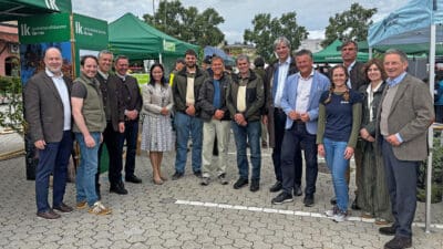 Gruppe von Männern und Frauen steht in einer Reihe vor Zelten auf einem Platz.