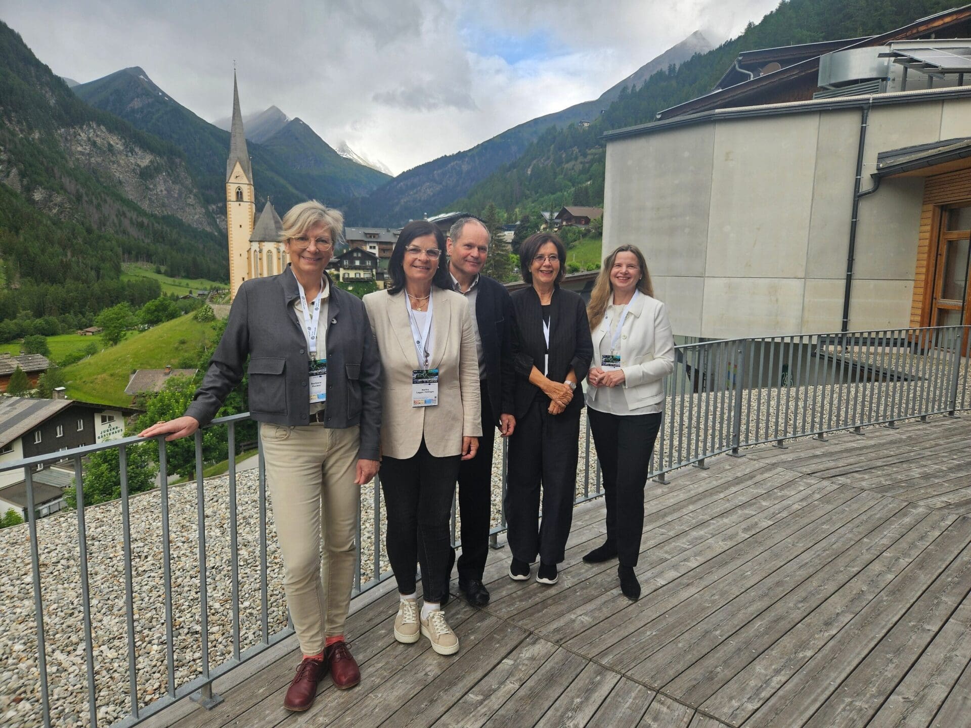 Fünf Personen stehen auf einer Holzterrasse vor Berglandschaft mit Kirche in Heiligenblut.
