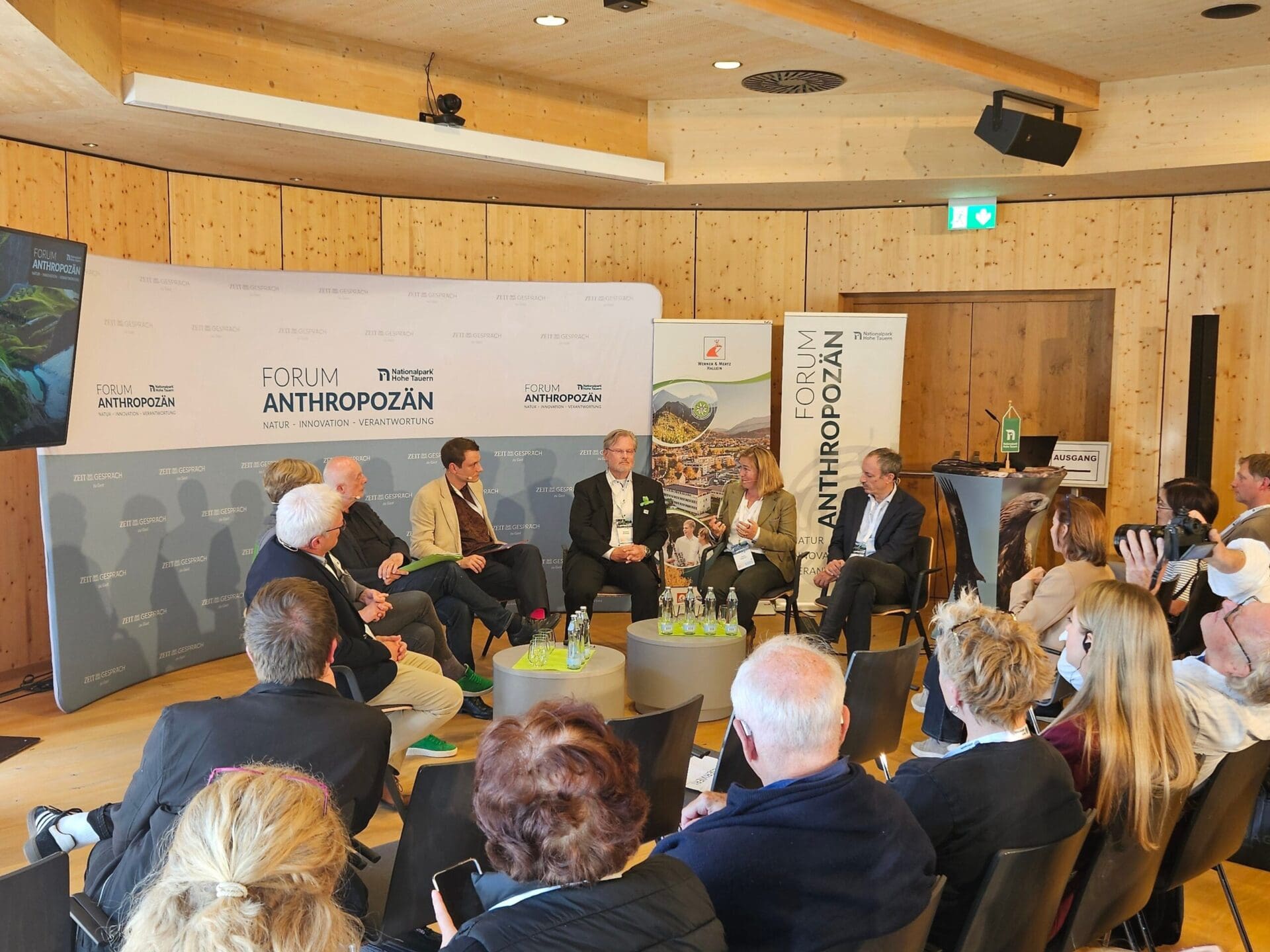 Diskussionsteilnehmer auf einer Bühne beim Forum Anthropozän in einem holzverkleideten Saal mit Publikum im Vordergrund