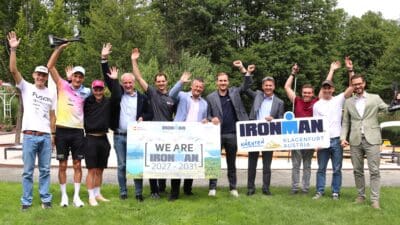 Gruppe von Männern bei IRONMAN Pressekonferenz mit erhobenen Armen und Schildern im Freien