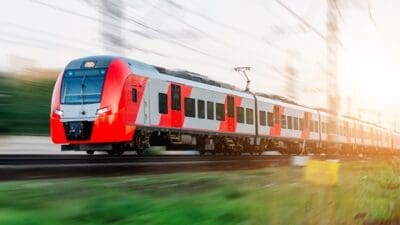 Roter und silberner Elektrotriebzug fährt mit hoher Geschwindigkeit auf Bahngleisen durch eine grüne Landschaft.