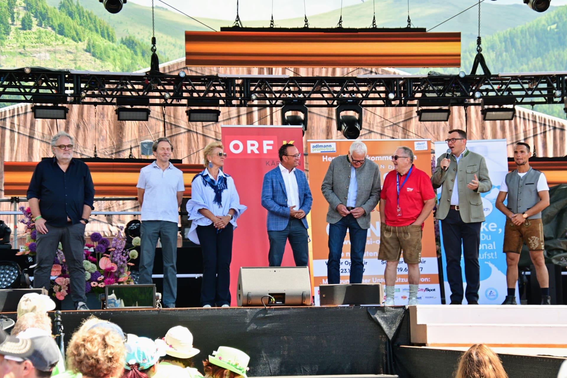 Mehrere Personen stehen auf einer Bühne vor Bergkulisse bei einer Veranstaltung.