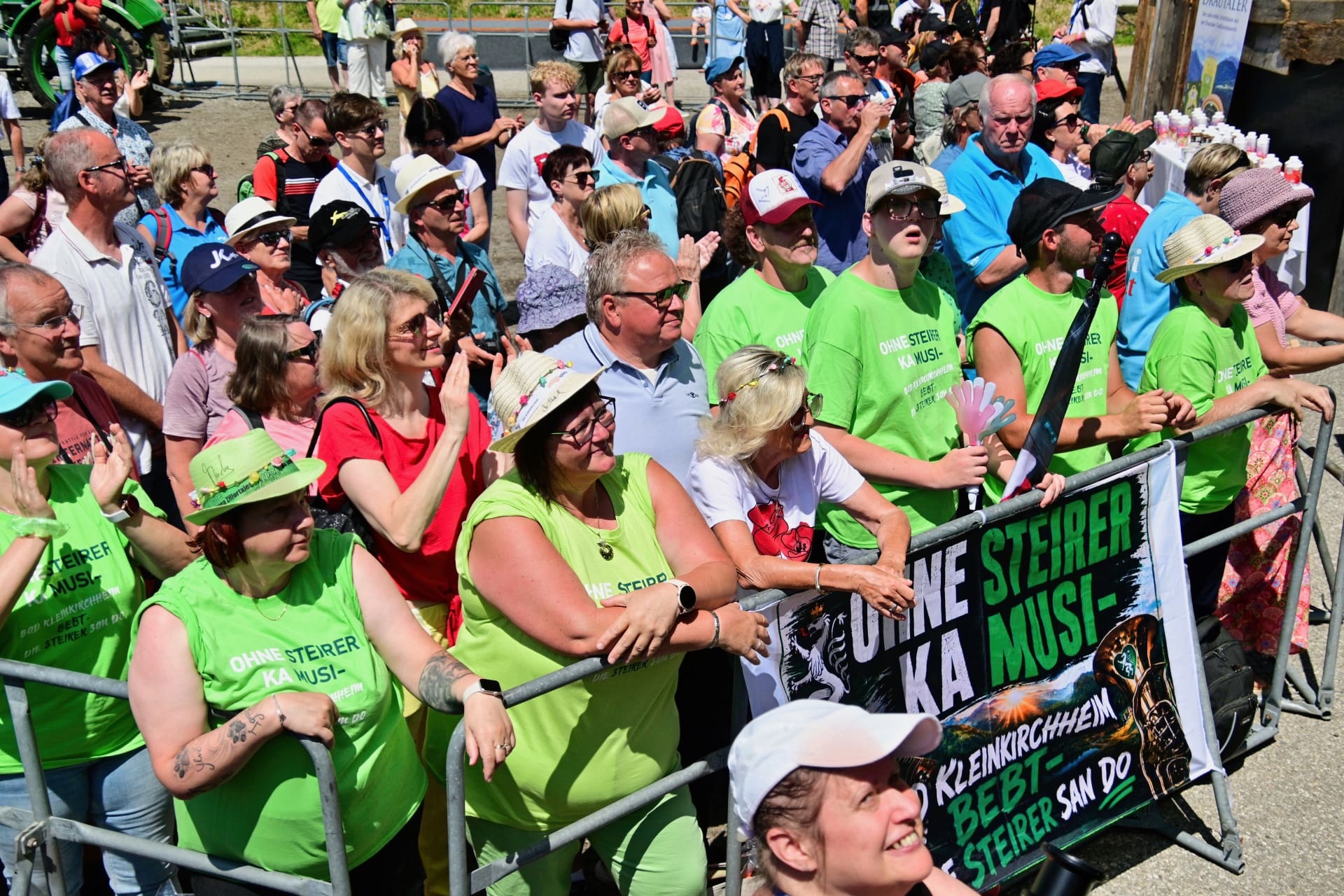 Menschenmenge in grünen Shirts hält Banner Ohne Steirer ka Musi bei Veranstaltung