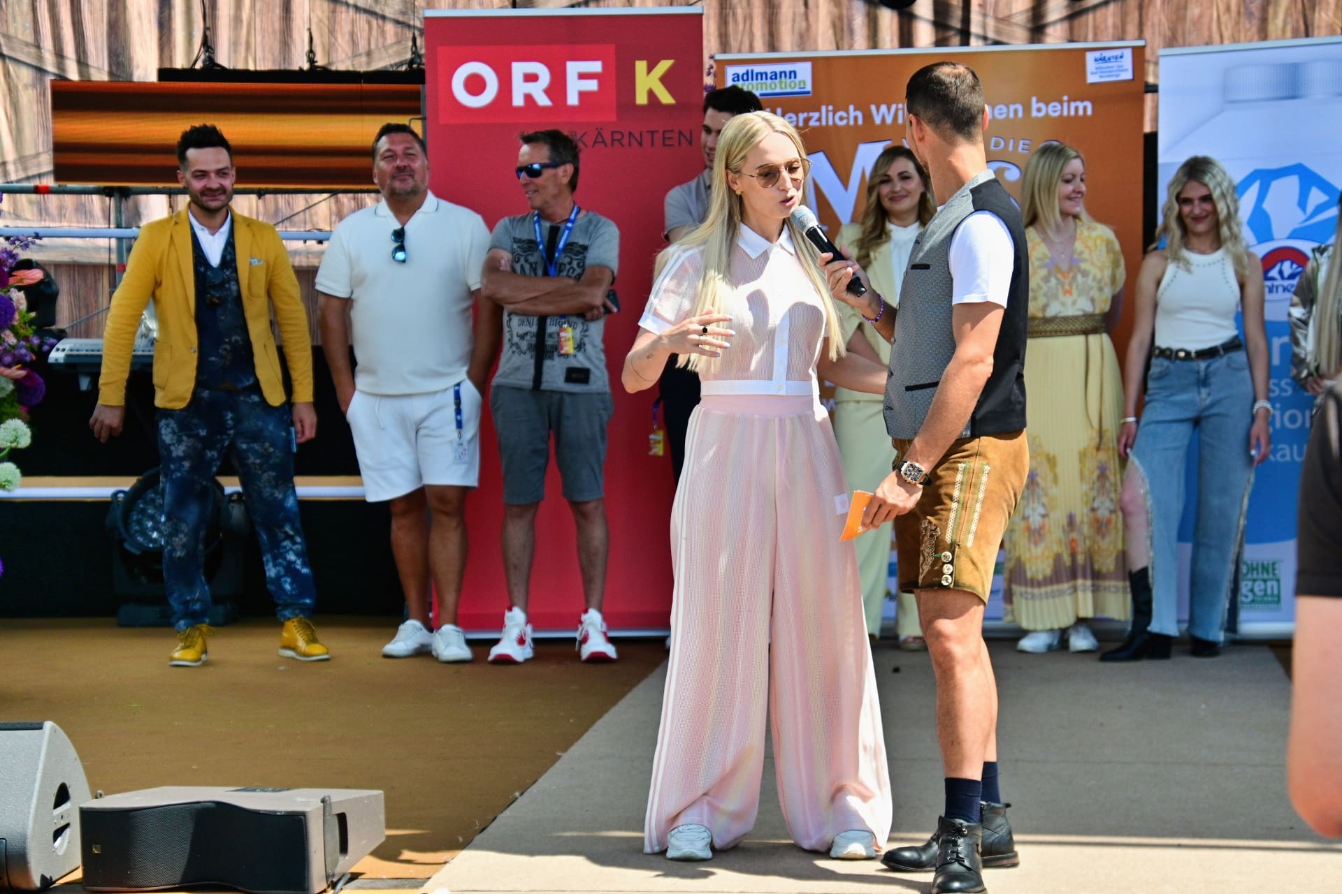 Blonde Moderatorin mit Mikrofon spricht mit Mann in Tracht auf Bühne vor ORF Banner