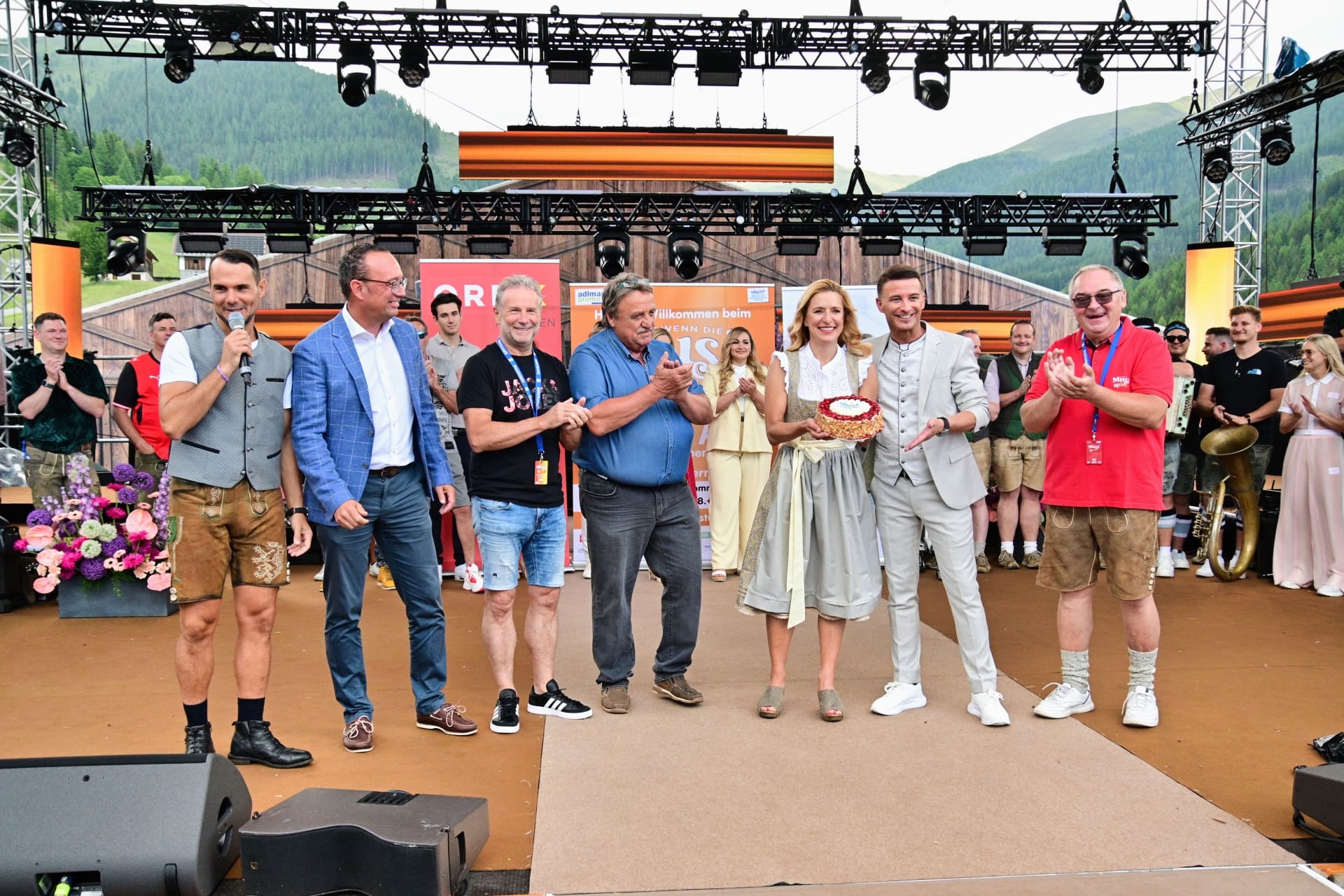 Gruppe von Personen auf einer Bühne bei einem Open-Air-Event in den Bergen mit einer Torte