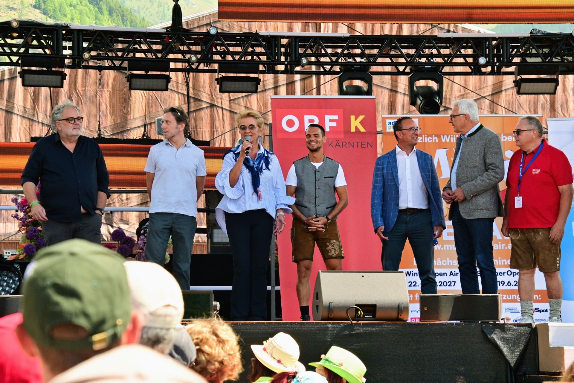 Eine Frau spricht in ein Mikrofon auf einer Bühne vor Publikum bei einer Veranstaltung.