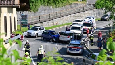 Blaues und silbernes Auto nach Kollision auf Straße mit Einsatzkräften und Zuschauern
