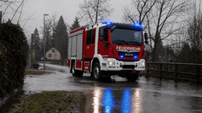 Rotes und weißes Feuerwehrfahrzeug mit blauem Blaulicht auf regennasser Landstraße