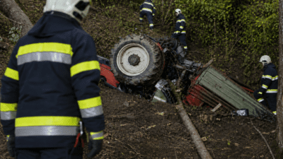 Feuerwehrleute sichern einen umgestürzten Traktor an einem bewaldeten Steilhang.