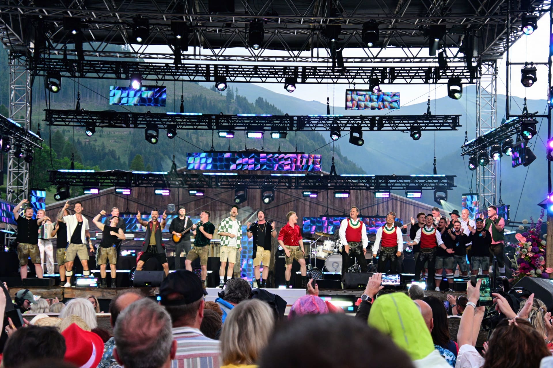 Viele Künstler auf der Bühne beim Sommer Open Air Festival mit Publikum und Bergpanorama im Hintergrund