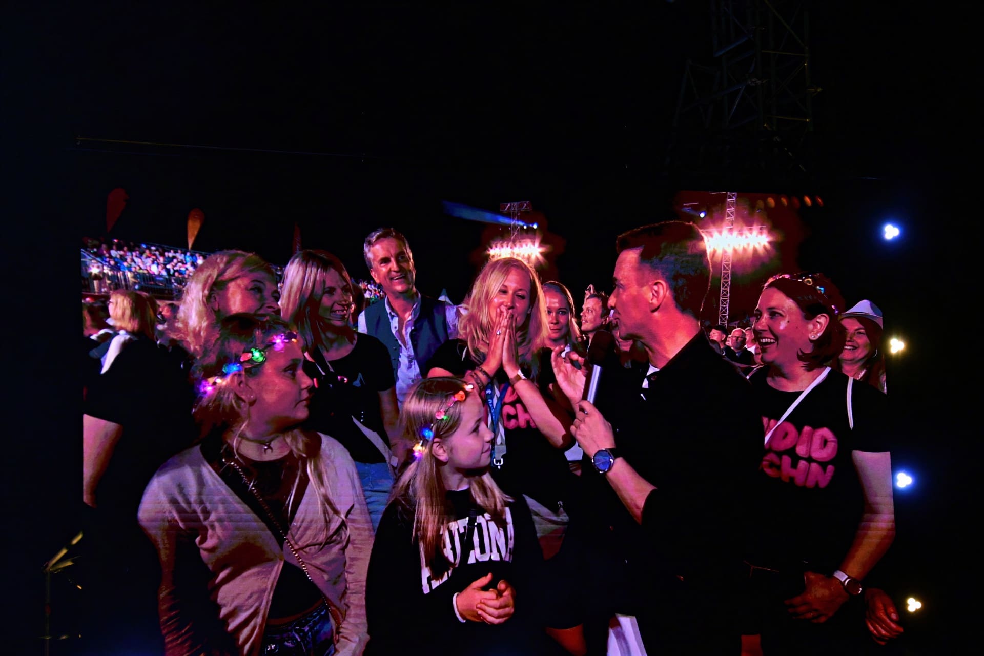 Moderator mit Mikrofon spricht mit Frau und Mädchen bei nächtlichem Open-Air-Konzert vor Publikum