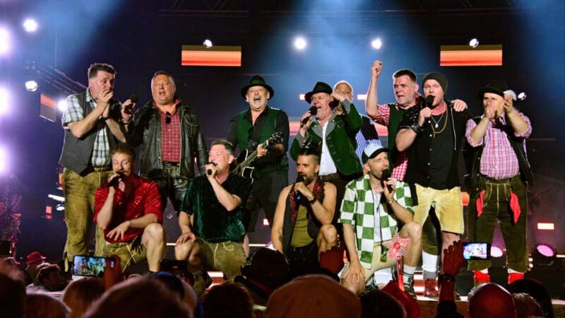 Gruppe von Sängern und Musikern auf einer beleuchteten Bühne vor Publikum