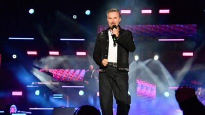 Sänger mit grauem Haar und Bart singt auf beleuchteter Bühne mit Rauch und Lichtern
