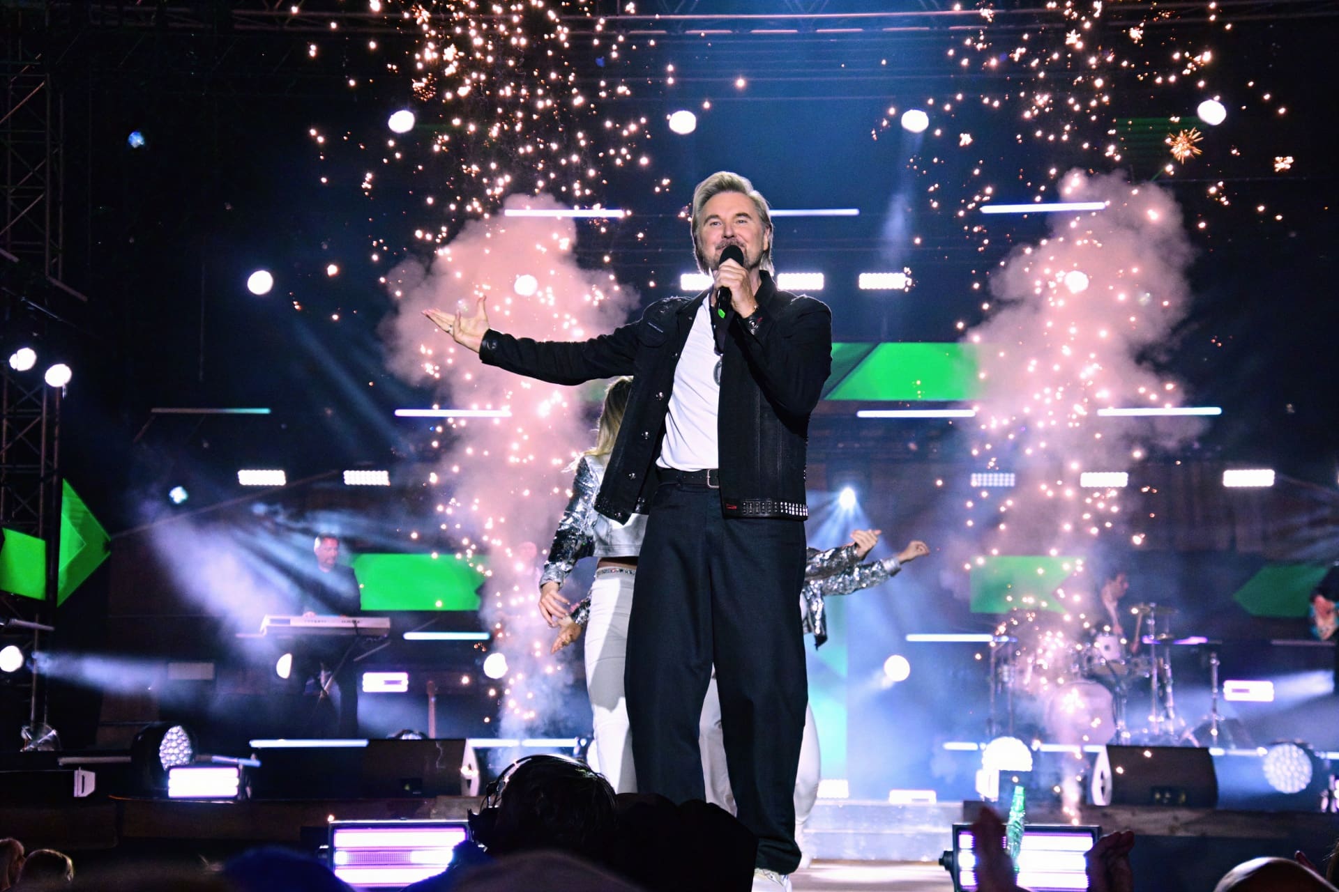 Sänger mit grauem Haar singt auf Bühne mit Pyrotechnik und Rauch