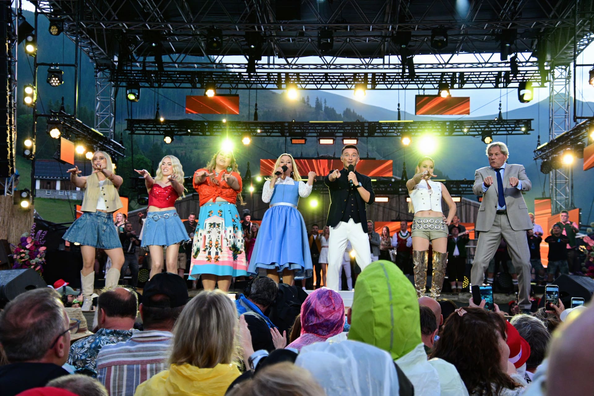 Mehrere Sängerinnen und Sänger stehen auf einer beleuchteten Bühne und singen vor Publikum.