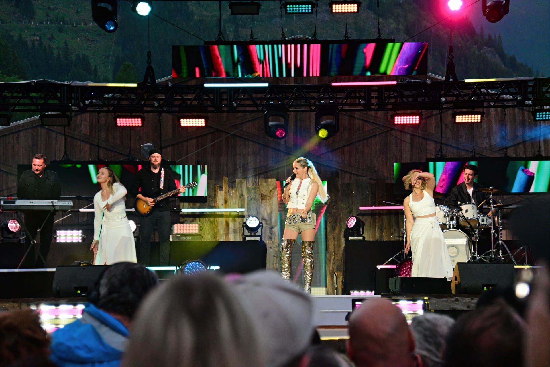 Sängerin mit Mikrofon auf beleuchteter Bühne bei Open-Air-Konzert mit Band und Publikum