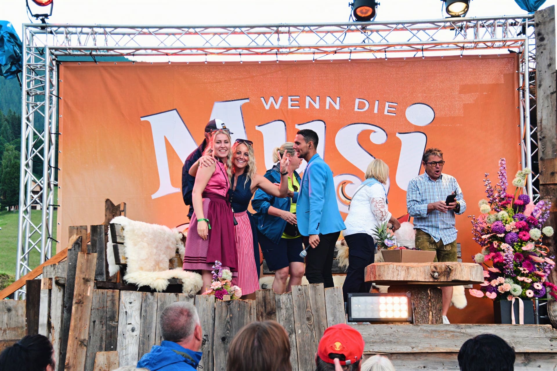Mehrere Personen stehen auf einer Bühne vor einem großen orangen Banner mit der Aufschrift Wenn die Musi