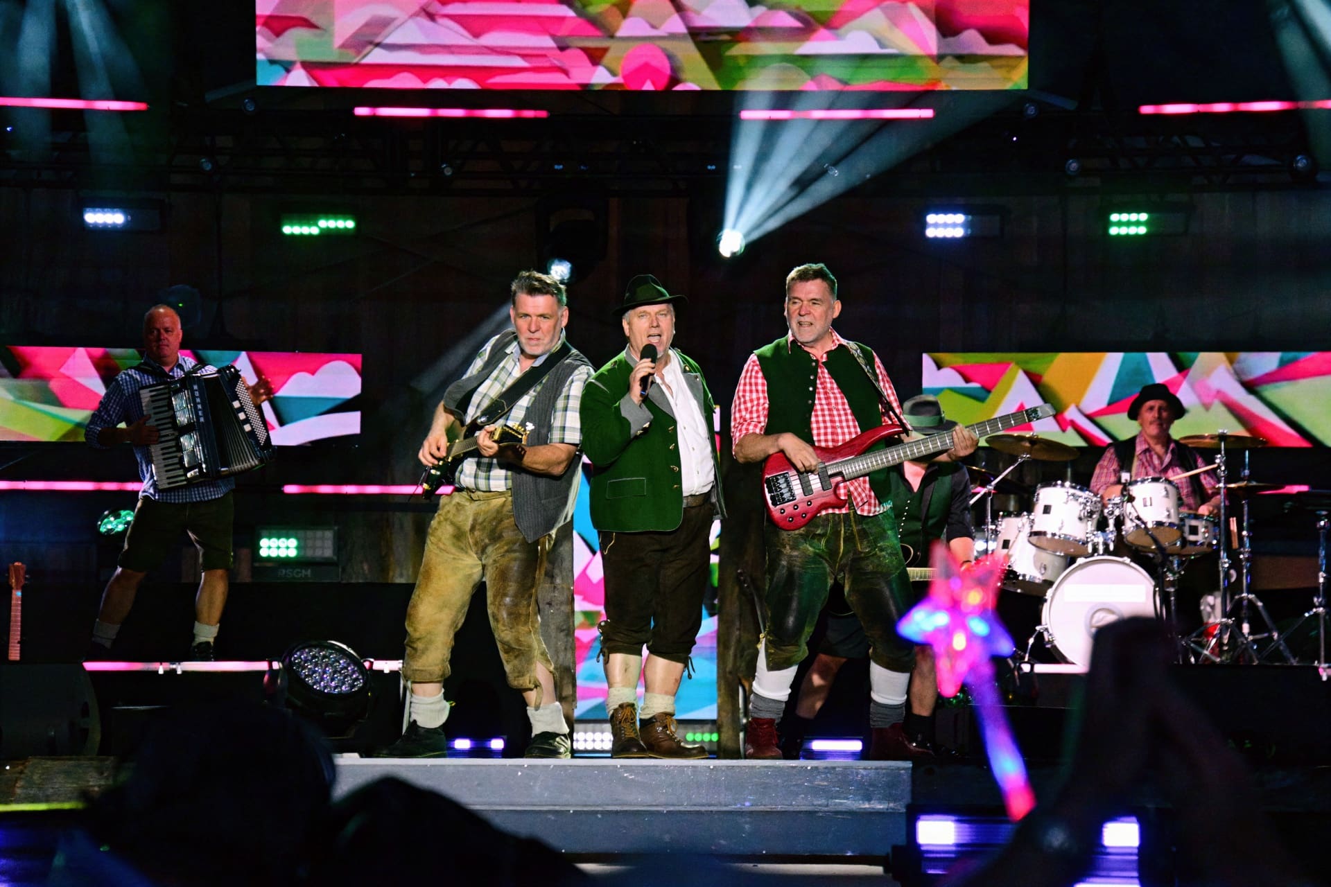 Mehrere Musiker in Tracht mit Instrumenten auf einer beleuchteten Bühne beim Open Air.