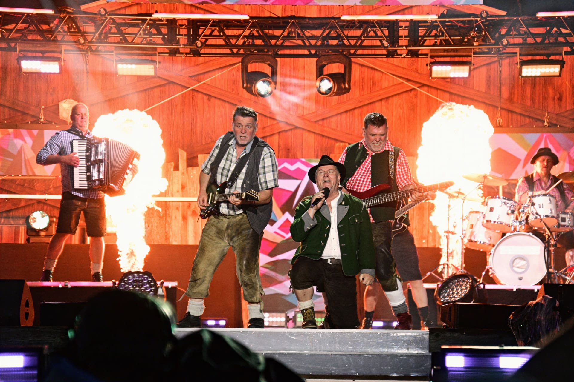 Musiker in Tracht auf einer Bühne mit Gitarren Akkordeon und Pyrotechnik bei einem Live-Konzert.