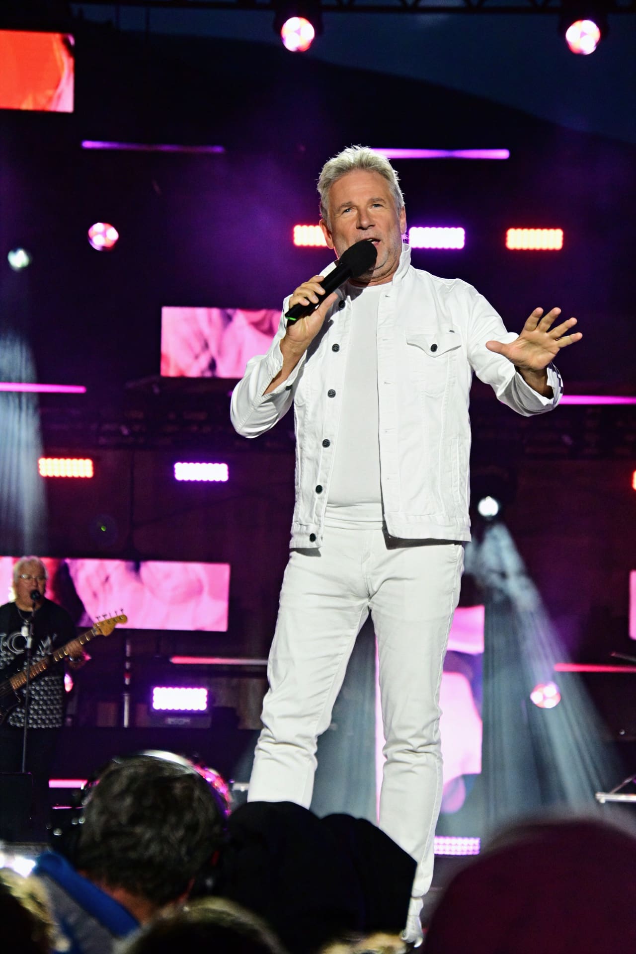 Sänger in weißer Jacke und Hose singt mit Mikrofon auf beleuchteter Bühne