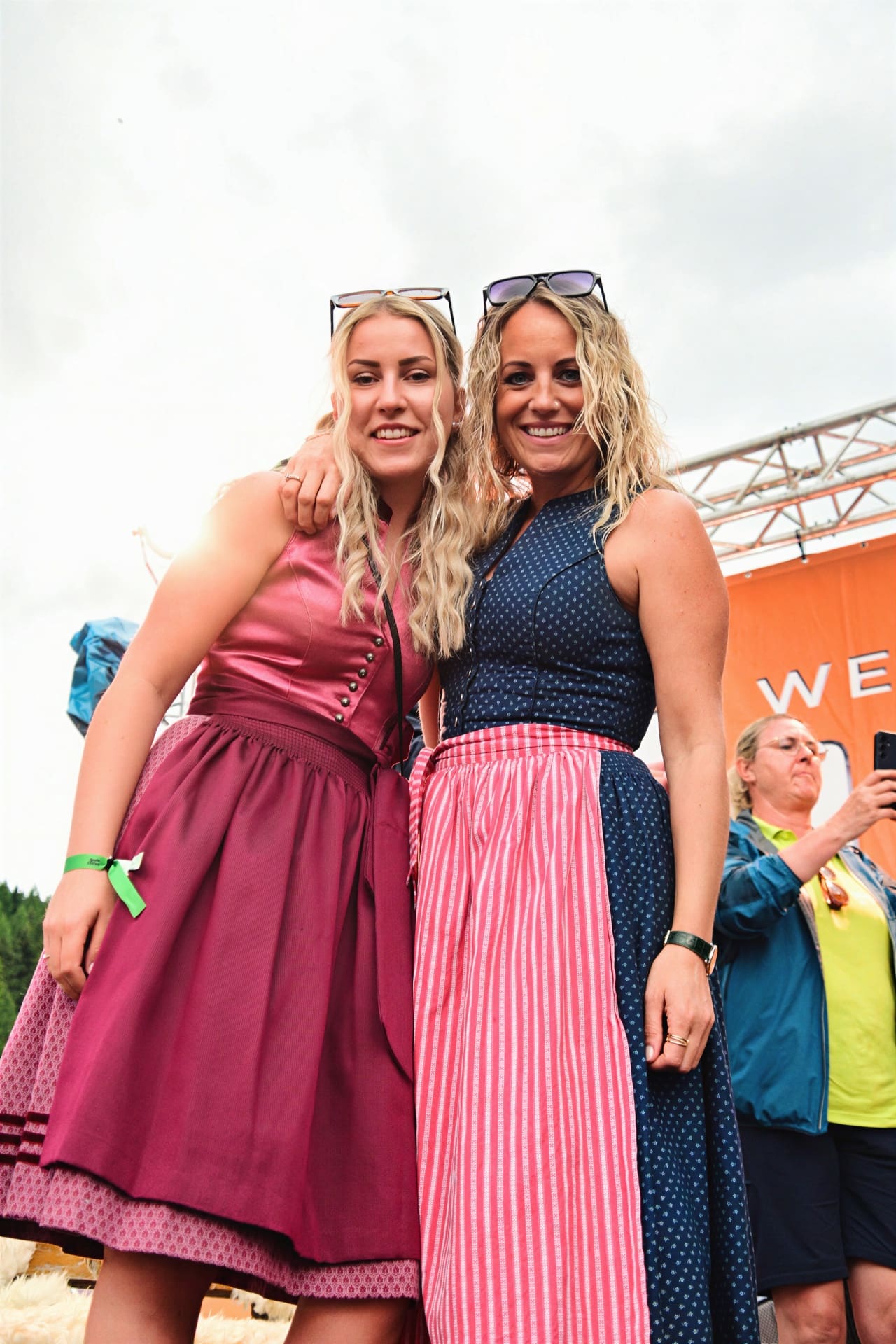 Zwei blonde Frauen in Dirndln lächeln eng umschlungen bei einem Open Air Festival