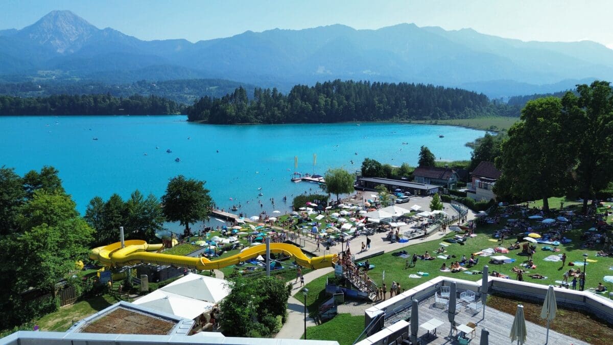 Blick auf den panoramabeach am Faaker See mit gelber Wasserrutsche und vielen Badegästen