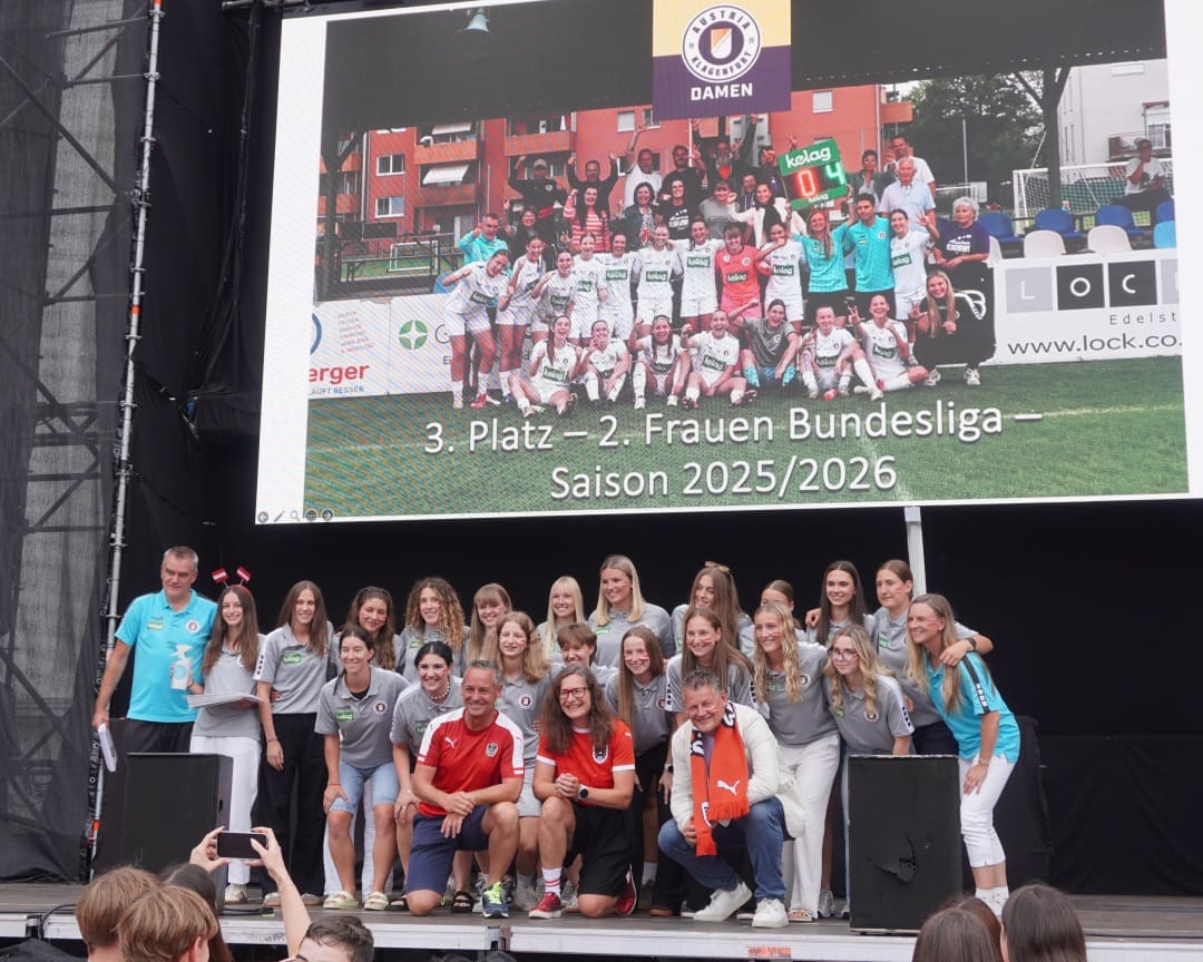 Gruppe von Fußballspielerinnen und Trainern auf einer Bühne vor einer großen Leinwand