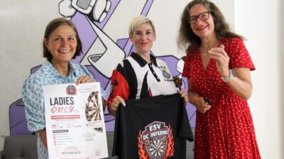 Drei Frauen präsentieren Poster und T-Shirt für Damenschnupperabend beim Dartsport