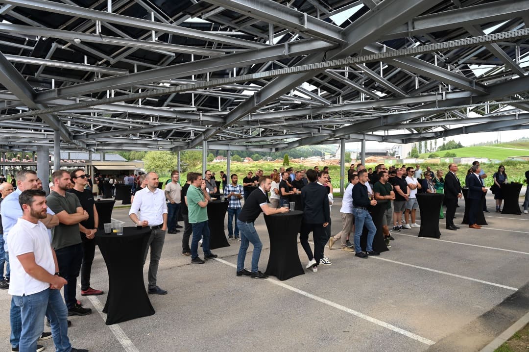 Menschen stehen bei der Eröffnung des Solarparks unter der Überdachung auf dem Firmengelände