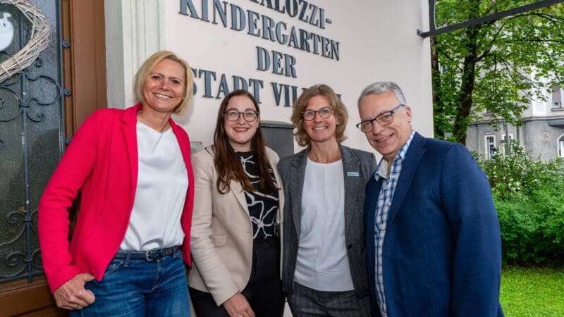Vier Personen stehen vor dem Eingang des Pestalozzi-Kindergartens der Stadt Villach.