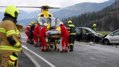 Rettungskräfte laden eine verletzte Person auf einer Trage in einen gelben Hubschrauber auf der Straße.