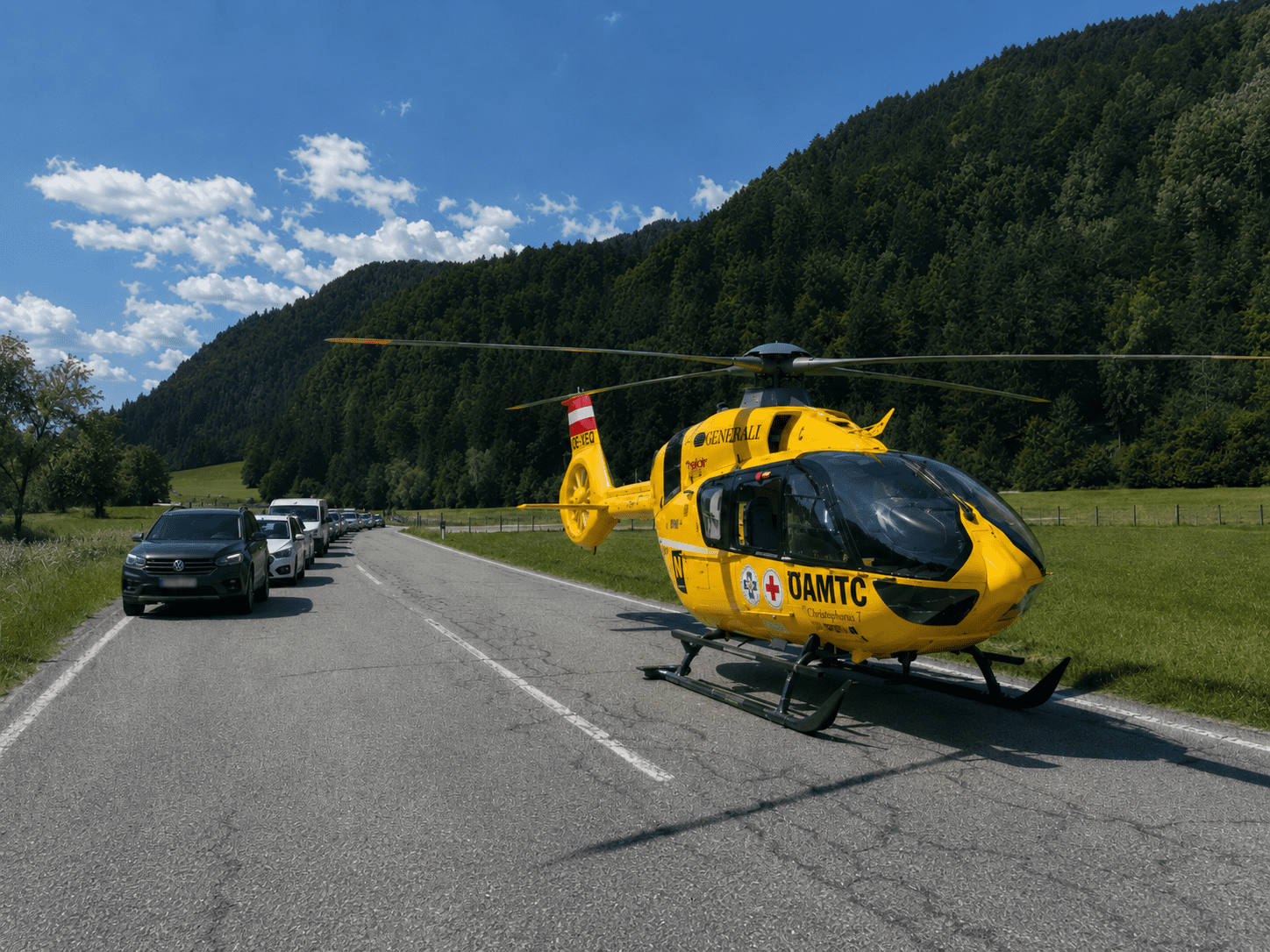 Gelber Rettungshubschrauber Christophorus 7 der ÖAMTC auf einer Landstraße mit wartenden Autos