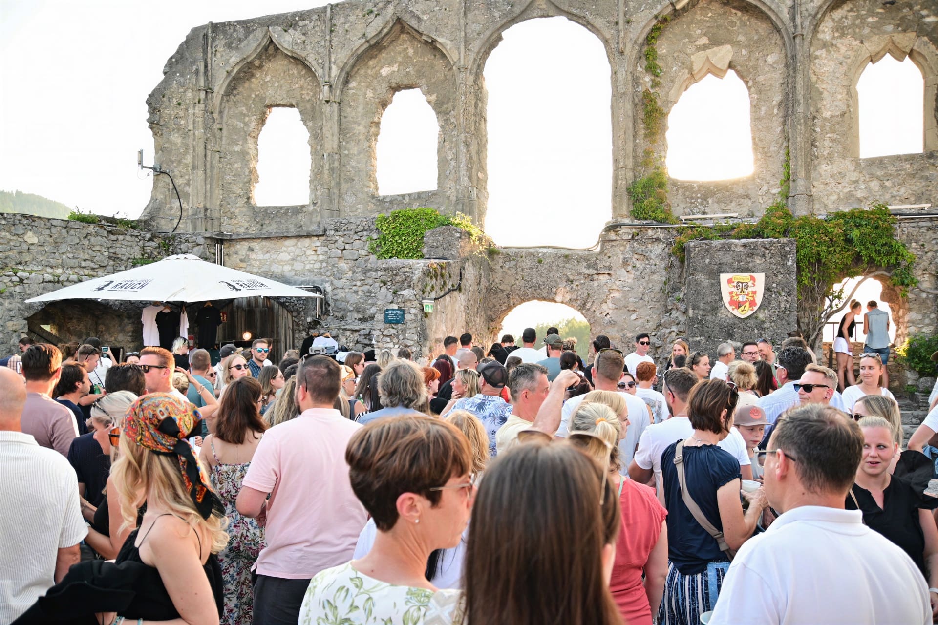 Menschenmenge versammelt vor historischer Steinruine mit großen Bögen und grünem Bewuchs bei einer Veranstaltung